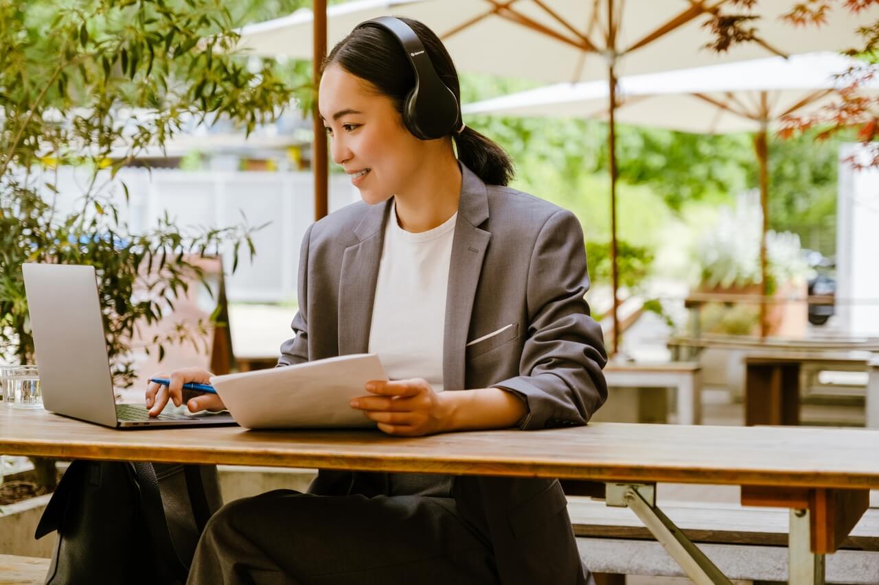 Woman Sitting at Outdoor Table with Headphones and Laptop